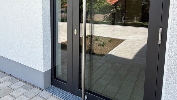 A modern sliding glass door with a metal handle, leading to a paved outdoor area. - Cozy vacation rental in the Allgäu region—perfect for families and couples (Sontheim)