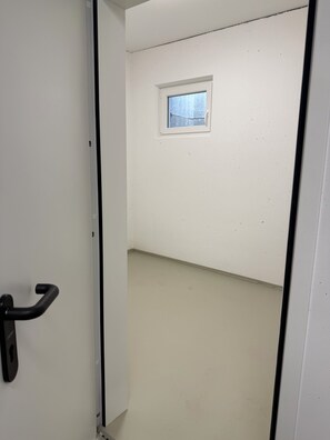 Ein schmaler Flur mit einer Tür links und einem kleinen Fenster rechts.