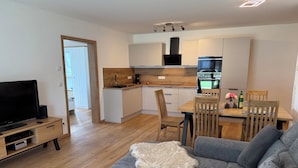 A modern living room with a grey sofa, a TV, and a wooden dining table with chairs. - Cozy vacation rental in the Allgäu region—perfect for families and couples (Sontheim)