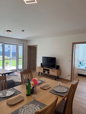 Una sala de estar moderna con comedor, televisor y puerta corrediza de vidrio que da a un balcón.