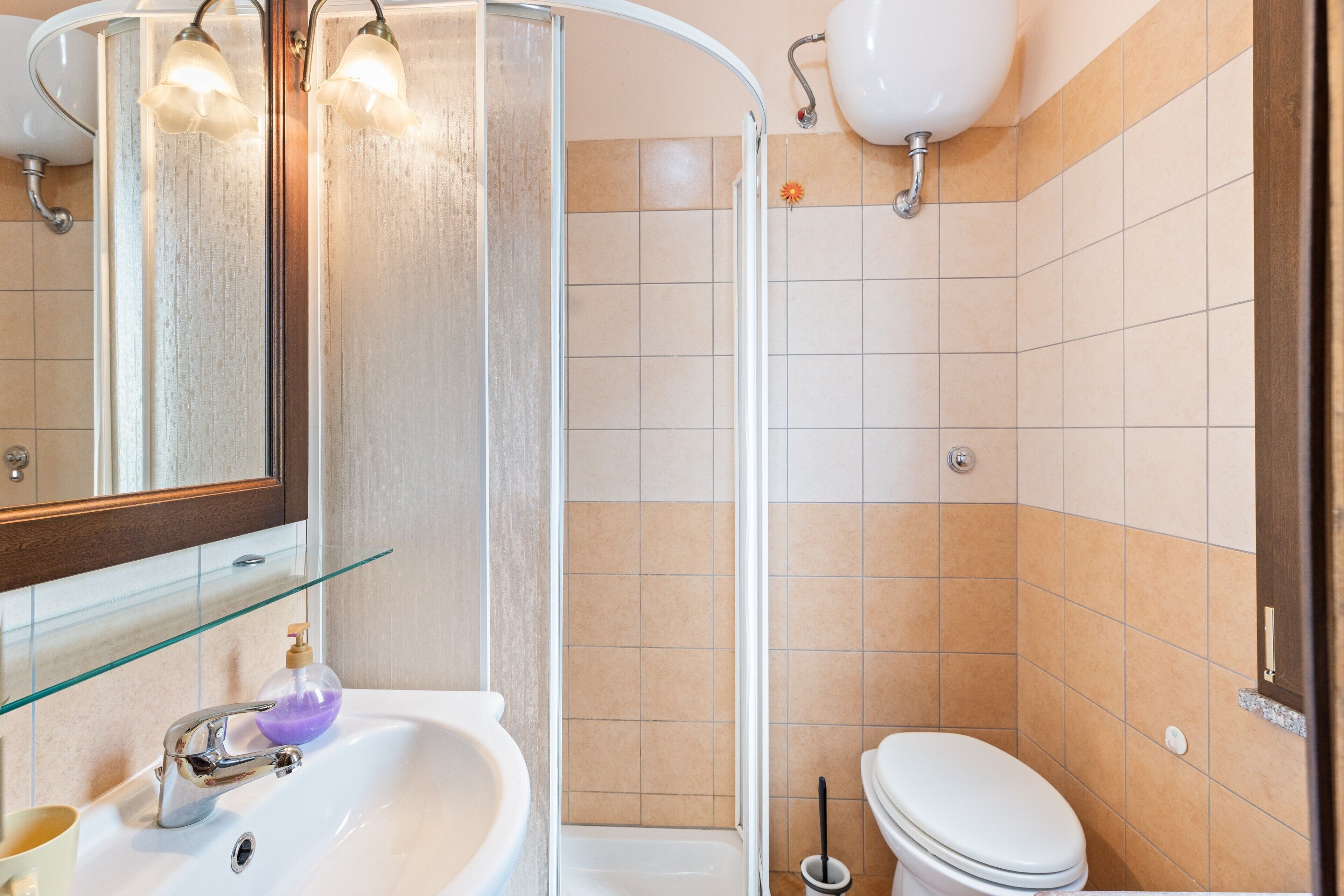 Ein Badezimmer mit Duschkabine aus Glas, Waschbecken in Weiß, Toilette und Spiegel mit Beleuchtung.