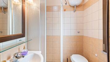 Ein Badezimmer mit Duschkabine aus Glas, Waschbecken in Weiß, Toilette und Spiegel mit Beleuchtung.