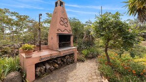 Una cocina rústica al aire libre con chimenea, sendero de piedra y vegetación circundante.