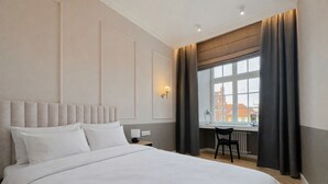 A hotel room with a large bed, a desk, and a view of buildings through the window. - AS HOME Rynek 265 (Wrocław)
