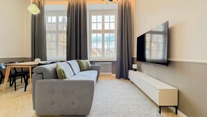 A modern living room with a sofa, a TV, a dining table, and large windows with curtains. - AS HOME Rynek 265 (Wrocław)