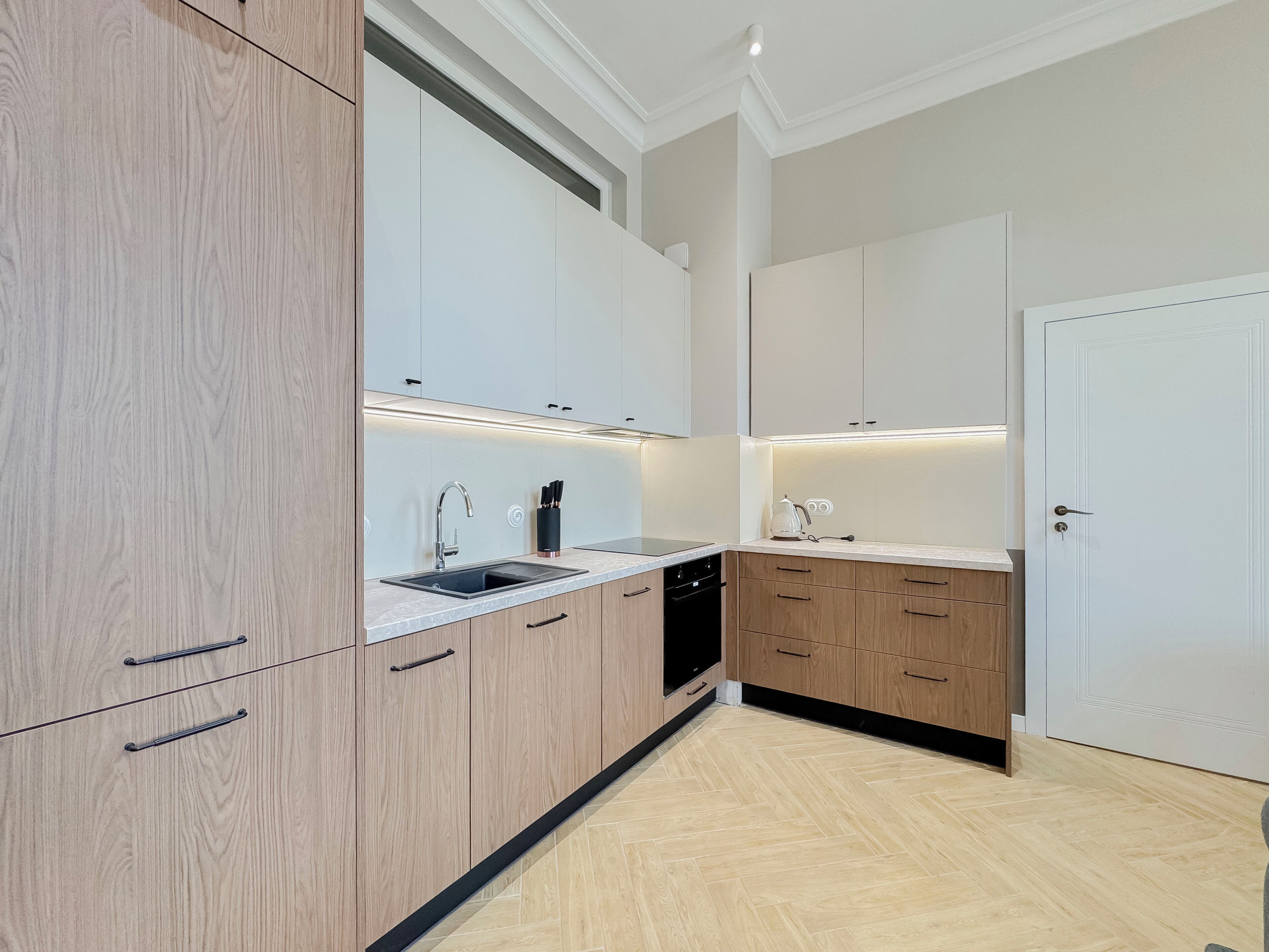 A modern kitchen with light wood cabinets, a stainless steel sink, and under-cabinet lighting.