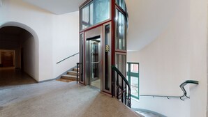 A staircase with a glass elevator door, carpeted floor, and a metal handrail. - AS HOME Rynek 265 (Wrocław)