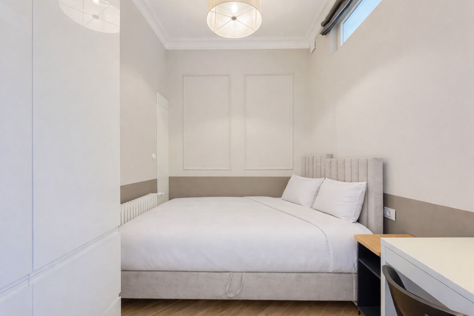 Un dormitorio con una cama, una mesita de noche, una silla, un radiador y una lámpara en el techo.