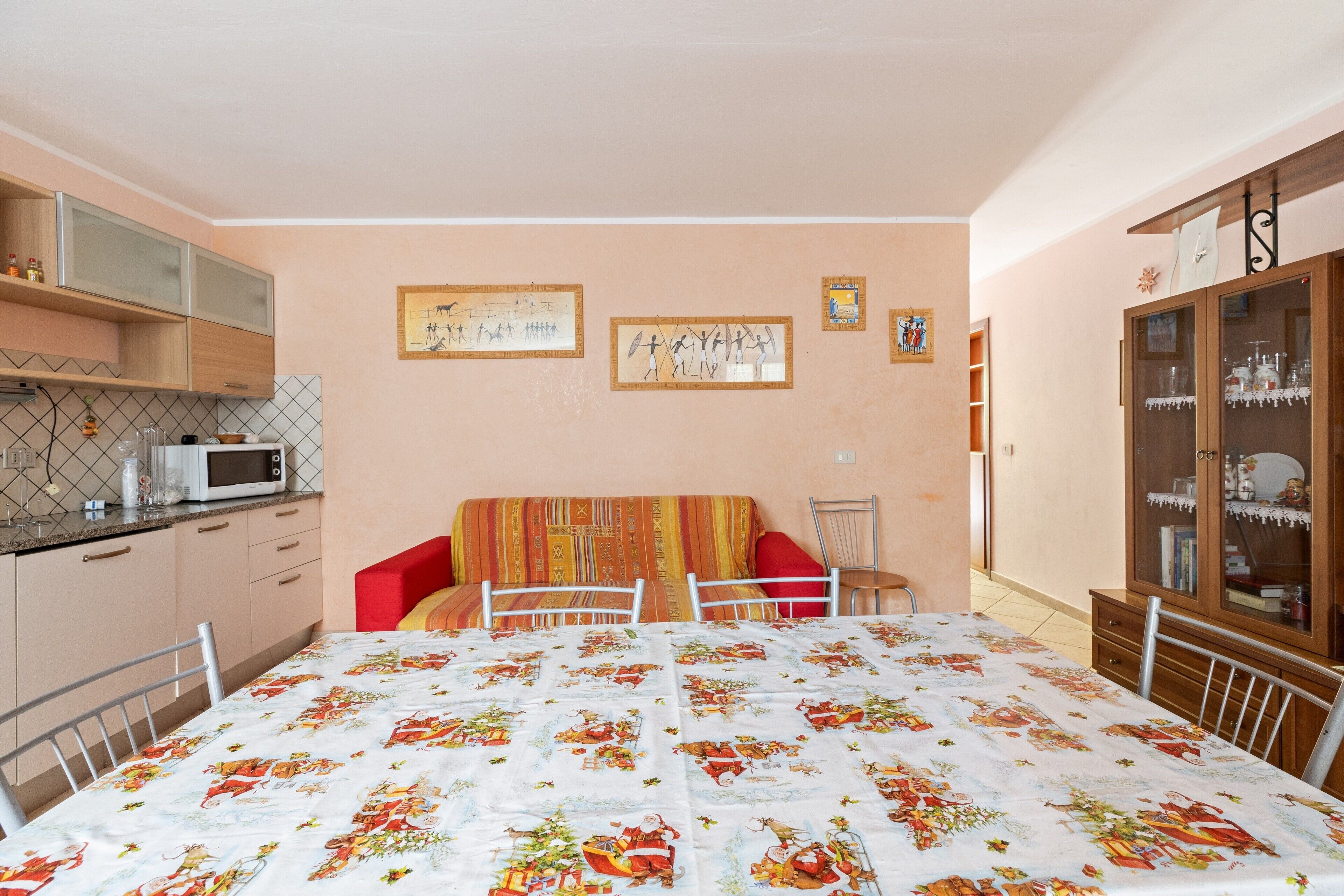 Une pièce de taille modeste comprenant un coin cuisine, une table à manger recouverte d’une nappe à motifs, un canapé rouge et un meuble avec des portes en verre.