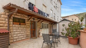 A courtyard with a stone wall, a wooden door, a small window, a table with chairs, and a potted plant. - Apartment 'Casa Anna - Bosa' with Air Conditioning (Bosa)