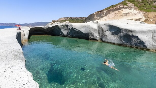 A clear pool with a rocky edge, a person swimming, and a distant view of the sea. - Apartment 'Casa Anna - Bosa' with Air Conditioning (Bosa)