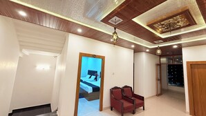 A hotel hallway with a reception desk, a bed in the background, and a red armchair.
