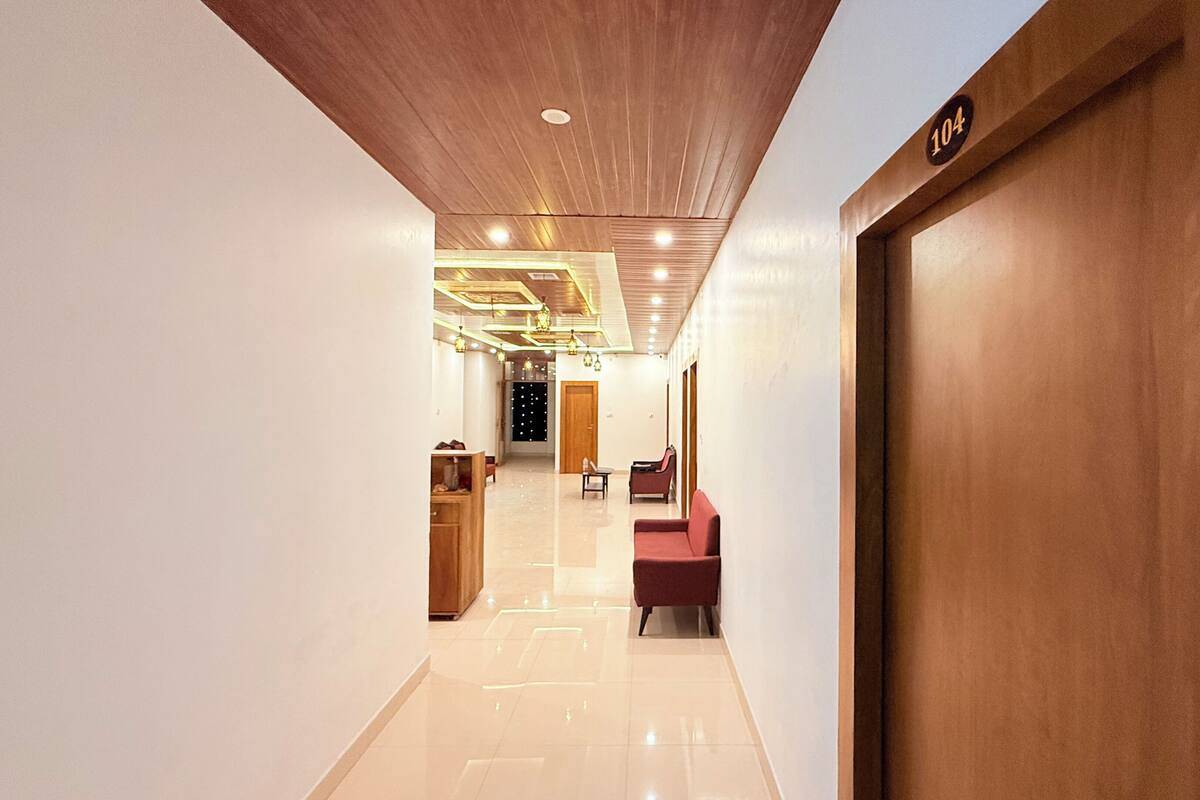 A modern hotel hallway with a wooden ceiling, a reception desk, a red chair, and a door marked with the number 104.