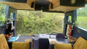 Um interior acolhedor com teto de madeira, uma mesa com cadeiras, um volante e vista para o verde lá fora.