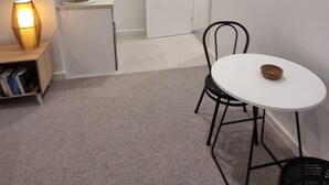 Et lille, kompakt rum med et hvidt bord og stole, en reol, en lampe og en dør til et andet rum.