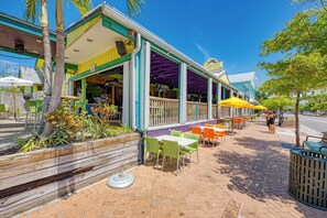 Ein Sitzbereich im Freien mit Tischen und Stühlen, eine überdachte Terrasse und ein Holz-Pflanzgefäß mit Pflanzen.