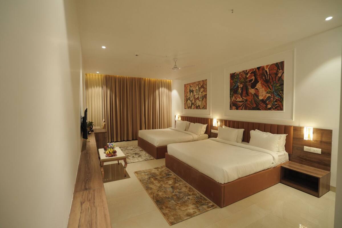 A hotel room with two beds, a TV, a desk, and artwork on the walls.