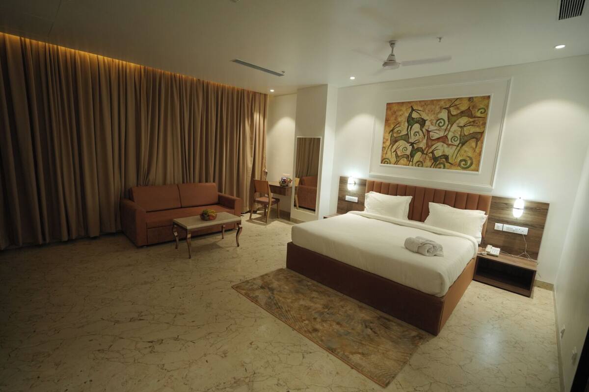 A hotel room with a bed, a sofa, a desk, and a large abstract painting on the wall.