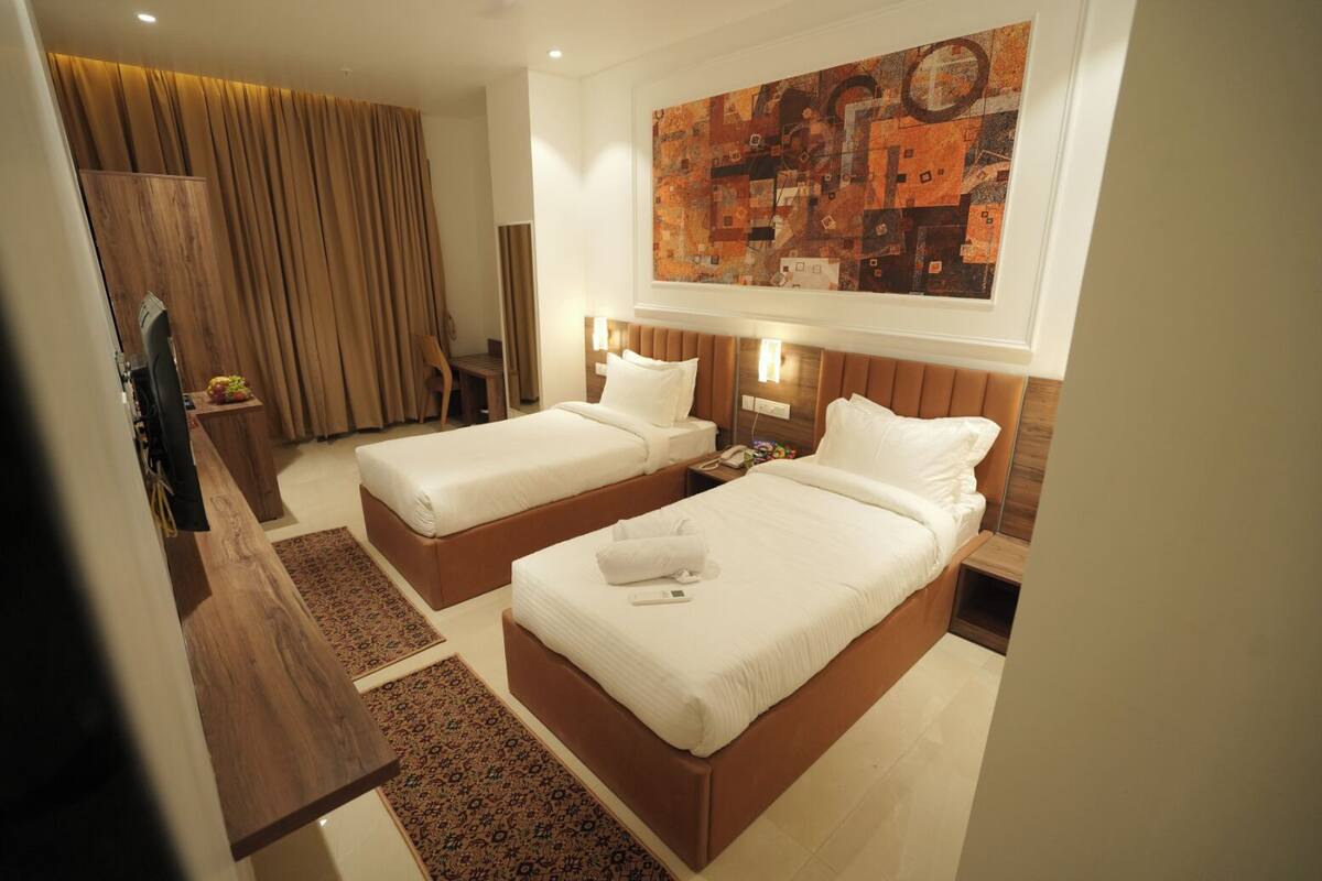 A hotel room with two beds, a wooden desk, a TV, and a large abstract painting on the wall.