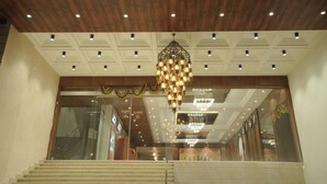 Un hall de hotel con techo de madera, una gran lámpara de araña y una escalera que conduce al piso superior.