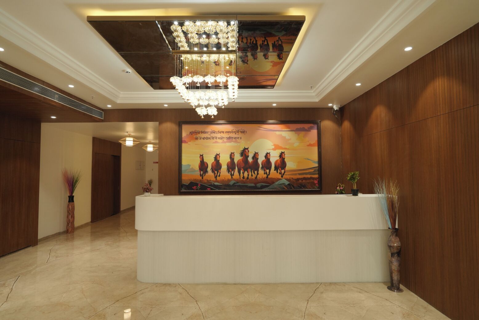A hotel reception area with a large reception desk, a chandelier, a mural of horses, and wooden paneling.