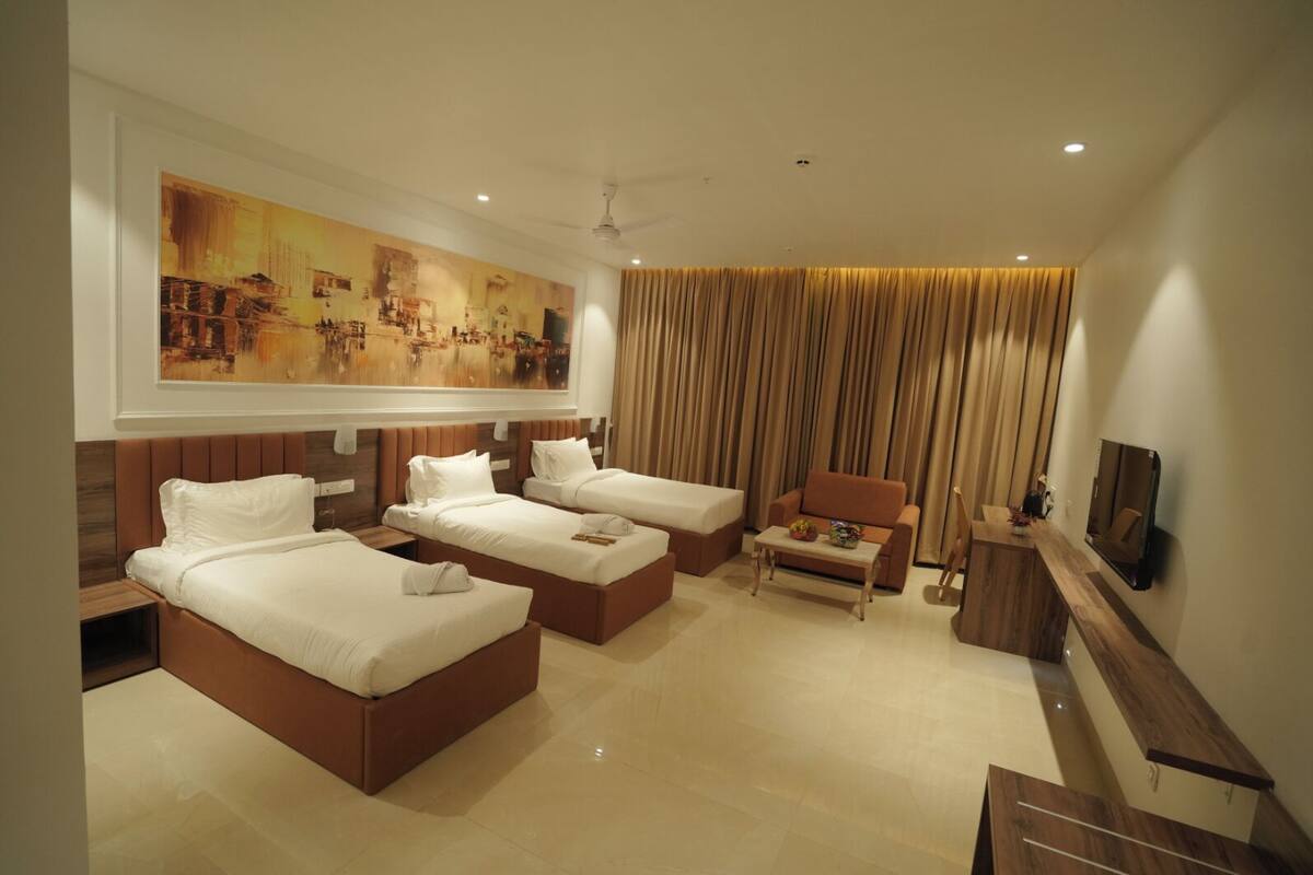 A hotel room with three beds, a sofa, a TV, and a large painting on the wall.