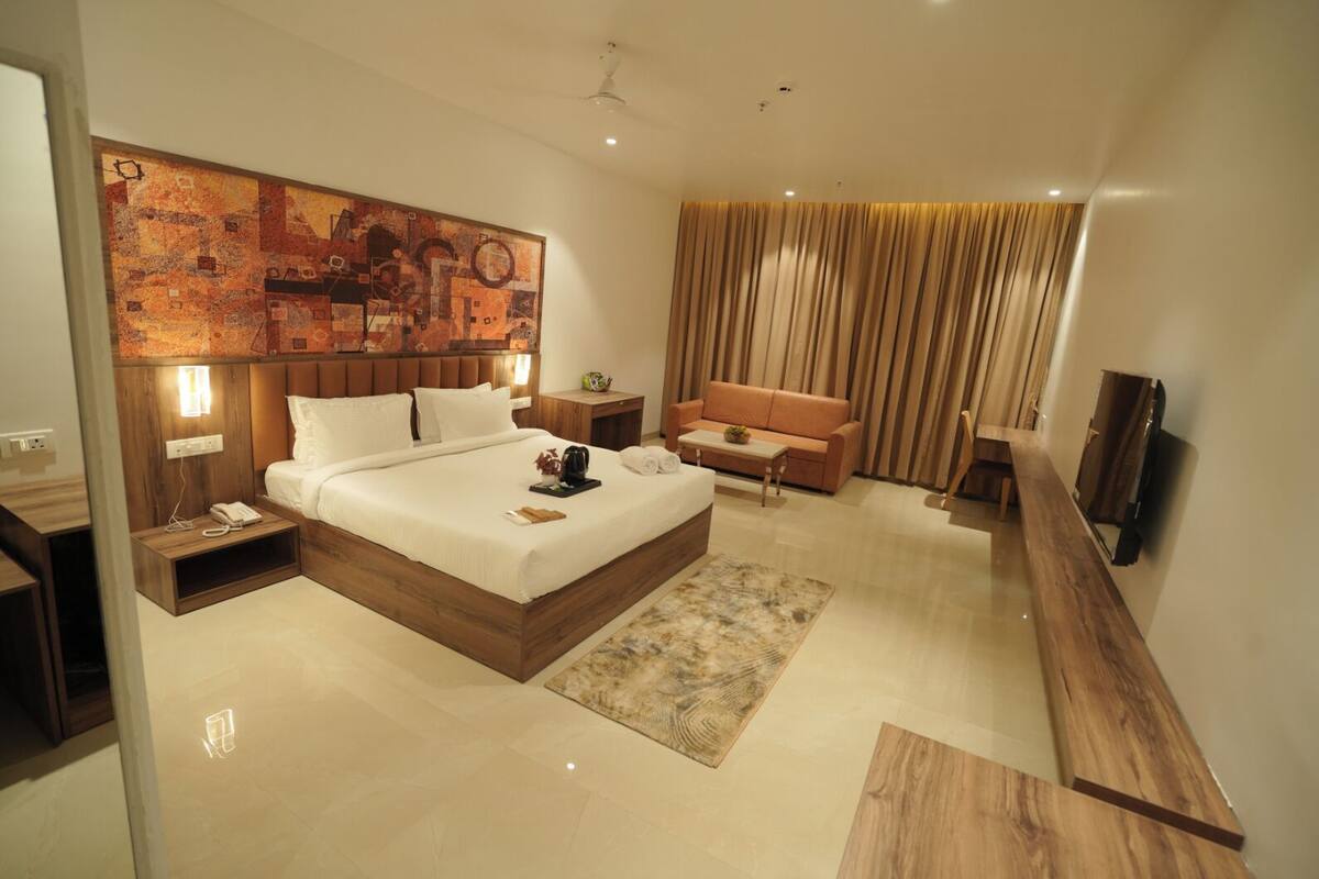 A modern hotel room with a large bed, a sofa, a TV, and a wooden headboard.