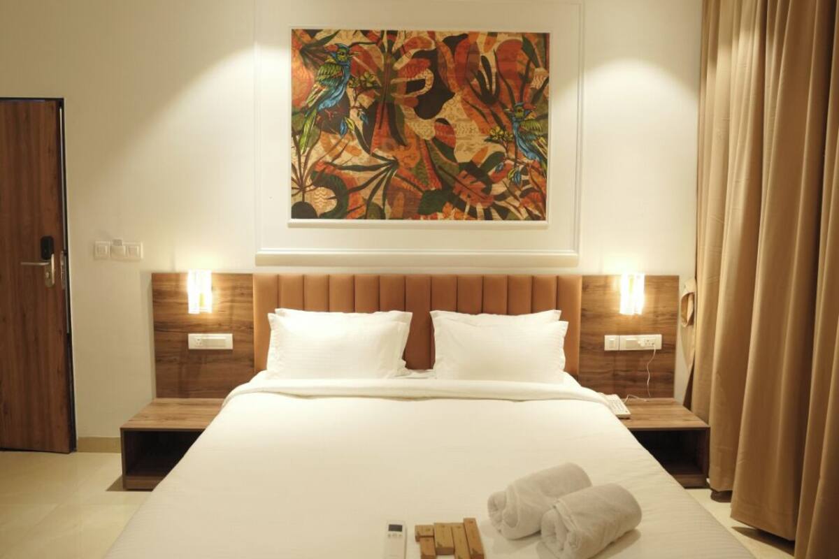 A hotel room with a large bed, a ceiling fan, a painting on the wall, and a window with curtains.
