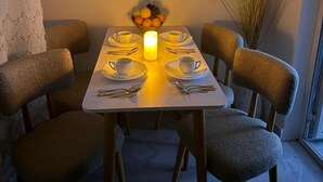 Una mesa de comedor con sillas, una vela encendida y jarrones de flores en la pared.