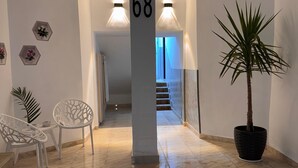 Un pasillo con un cartel con el número 68, una planta en maceta y dos sillas blancas.