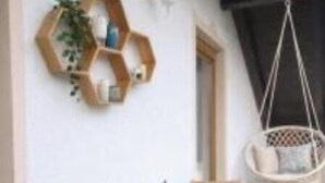 Eine Terrasse mit Holztisch und -stühlen, einem Hängesessel und einem sechseckigen Regal mit Gegenständen an der Wand.