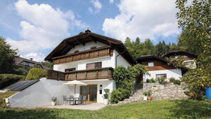 Uma casa de dois andares com uma varanda, um pátio com móveis de exterior e uma parede de pedra.