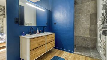 Un bagno con una parete blu, un lavandino bianco con cassetti in legno, uno specchio e uno spazio doccia.