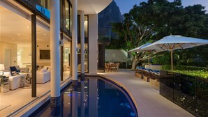 Un área moderna junto a la piscina con una pileta curvada, mobiliario exterior y vista a la montaña.