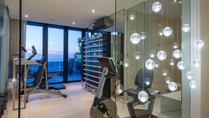 Un gimnasio moderno con equipo de ejercicio, un ventanal grande y una lámpara esférica distintiva.