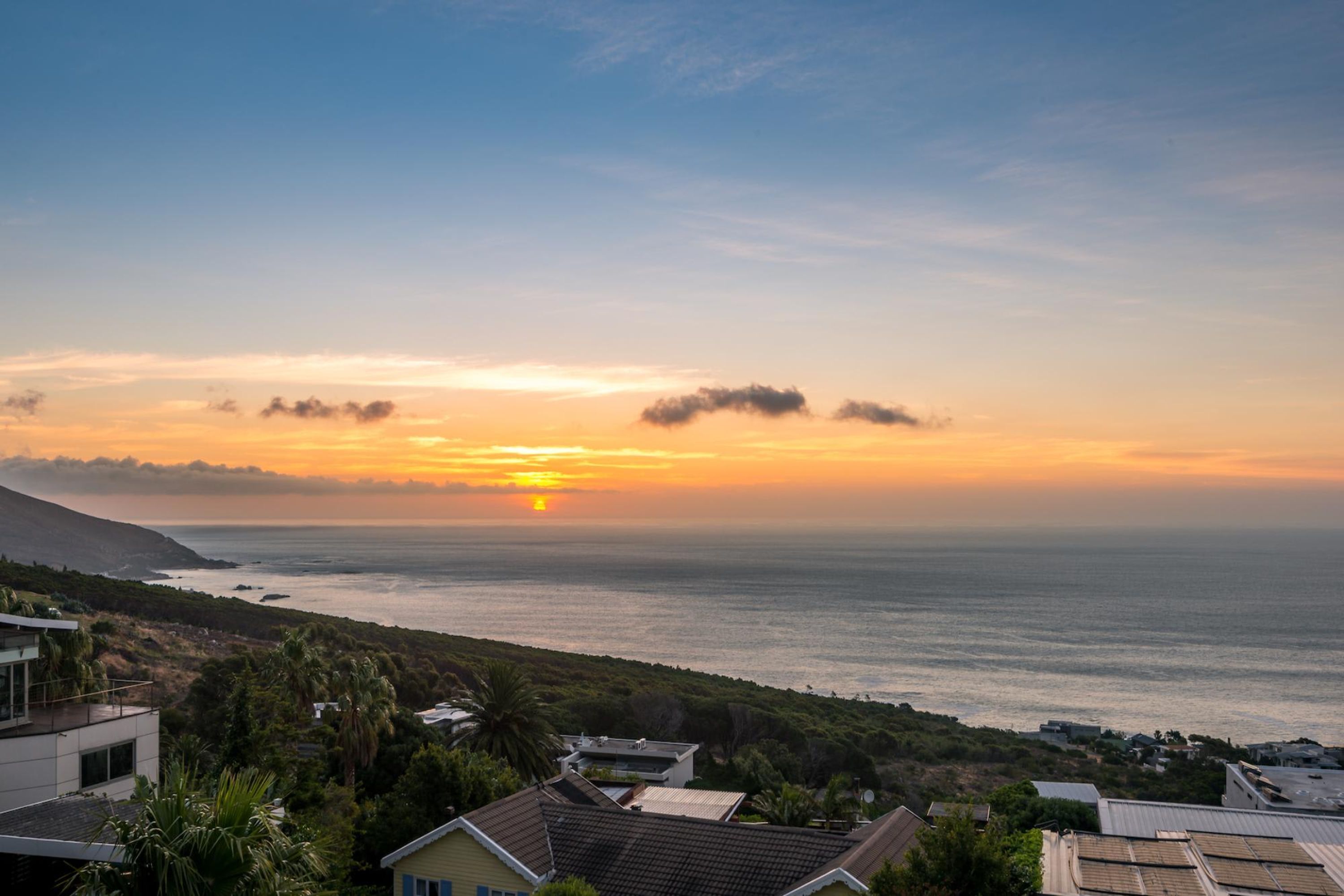 A coastal landscape with a sunset, houses, and a view of the ocean.