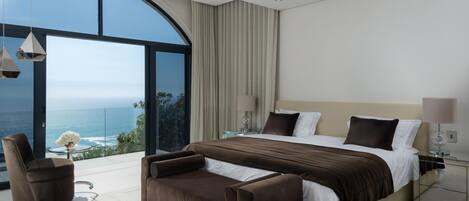 A modern bedroom with a large curved window, a bed, a sofa, and a small table.