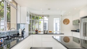A modern kitchen with white cabinets, a black countertop, and a large window. - Camps Bay 6bed w Ocean Views and Pool Villa Sevara (Cape Town)