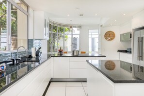 A modern kitchen with white cabinets, a black countertop, and a large window. - Camps Bay 6bed w Ocean Views and Pool Villa Sevara (Cape Town)