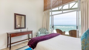 A bedroom with a bed, a nightstand, a mirror, a window with a view of the ocean, and a chair. - Camps Bay 6bed w Ocean Views and Pool Villa Sevara (Cape Town)