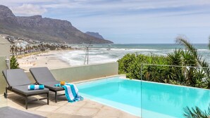 A pool with two lounge chairs, a view of the ocean, and a mountainous backdrop. - Camps Bay 6bed w Ocean Views and Pool Villa Sevara (Cape Town)
