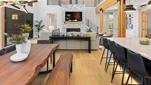 Ein modernes Wohnzimmer mit Kamin, Holzbalken, einer Essecke und einer Treppe.