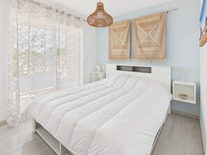 Een slaapkamer met een groot bed, een raam met dunne gordijnen, een rotan hanglamp en twee wandpanelen van geweven materiaal.