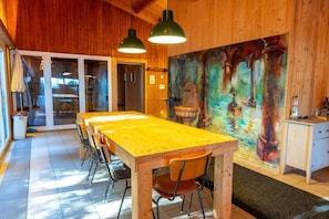 Un intérieur en bois avec une longue table et des chaises, un tableau au mur et une petite cuisine.