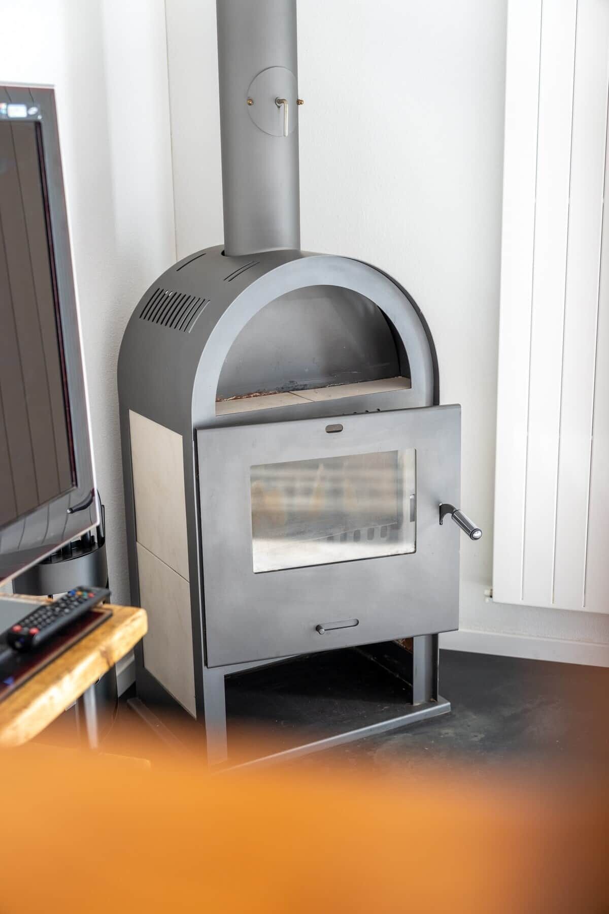 A modern wood stove with a glass door, a control panel, and a remote control on a wooden stand.