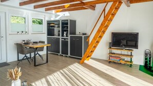 Quarto estilo loft com área de refeições, armários de cozinha, uma TV sobre um suporte de madeira e uma escada de madeira.