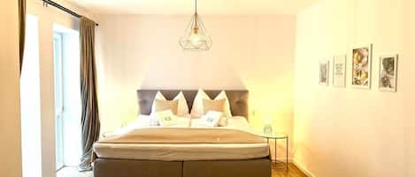 A bedroom with a bed, a geometric ceiling light, a bedside table, and a wall with framed pictures.