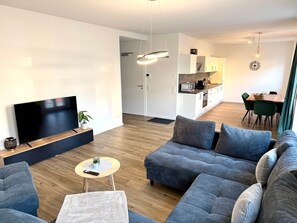 Een moderne woonkamer met een flatscreen televisie, banken, een salontafel en een eethoek met een tafel en stoelen.