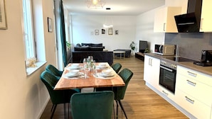 A modern kitchen with a dining area, wooden table, green chairs, and a hanging light fixture. - VetterLux Bellevue, suite, citycenter Ravensburg (Ravensburg)