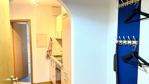 Un couloir avec un plancher en bois, un banc, un porte-manteau et un coin cuisine équipé de placards et d’un évier.